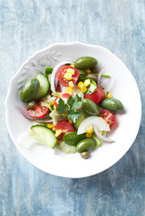 Healthy salad with green olives, sweet corn, cherry tomatoes, red onion, baby spinach, capers and fresh herbs. Bright wooden background. Top view.