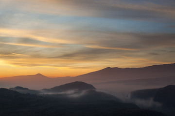 Valley filled with soft mist, distant silhouettes of impressive mountains and amazing colors of vivid morning sky