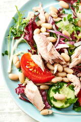  Healthy salad with tuna, cannellini bean, endive and tomatoes. Bright wooden background. Top view. 