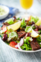 Tasty salad with grilled beef steak, cherry tomatoes and lettuce. White wooden background. Close up.