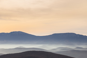 Pastel color palette of misty landscape with rocky mountain peak rising above fog covered valleys and mountain layers during colorful 