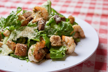 Cesar salad with grilled shrimp, croutons and Parmesan cheese in single plate table setting