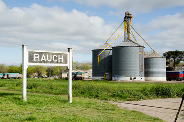 Sign with the name of the village and rural silos, at the train station, in Rauch, Buenos Aires,...