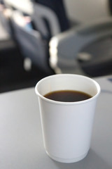 A fresh and hot cup of black coffee served on a folded out airplane seat tray