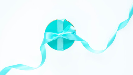 Turquoise aquamarine round gift box with bow and ribbon isolated on white backdrop. Festive party flat lay. Copy space