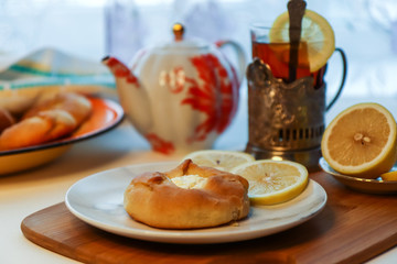 Cosy breakfast concept, transparent cup of tea with lemon and pastry on white background, near the window, front view, horizontal