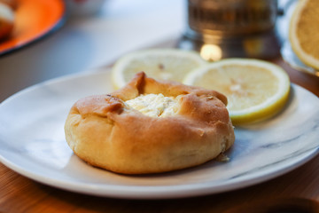 Cosy breakfast concept, transparent cup of tea with lemon and pastry on white background, near the window, front view, horizontal
