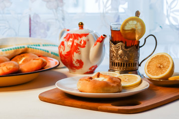 Cosy breakfast concept, transparent cup of tea with lemon and pastry on white background, near the window, front view, horizontal