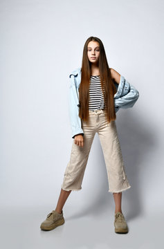 Teenager in striped t-shirt, sneakers, denim jacket and pants. She is pointing at you, posing isolated on white. Full length