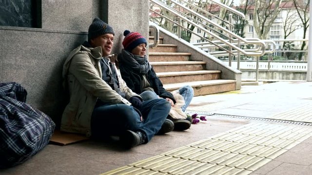 homeless people ask for alms sitting on the sidewalk against the wall