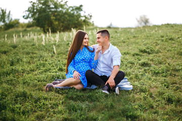 a married couple sitting on the lawn spreading a blanket, a pregnant girl and her loving boyfriend