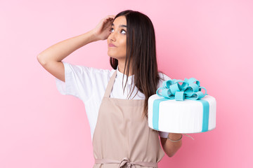 Young woman with a big cake over isolated background having doubts and with confuse face expression