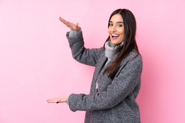 Young brunette woman over isolated pink background holding copyspace to insert an ad