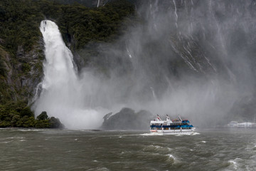 Tour boat passing gushing waterfall at Milford Sound, New Zealand