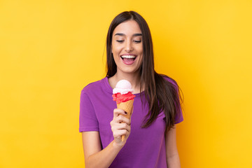Young brunette woman with a cornet ice cream over isolated yellow background