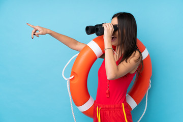 Lifeguard woman over isolated blue background with lifeguard equipment and with binoculars while...