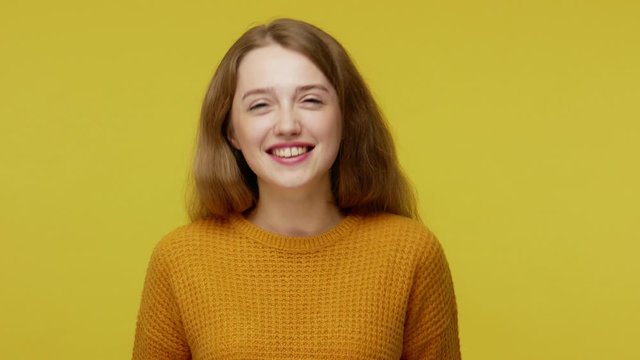 Childish disobedient behavior. Playful young woman with brown hair in pullover sticking out tongue at camera, teasing with naughty foolish expression. indoor studio shot isolated on yellow background