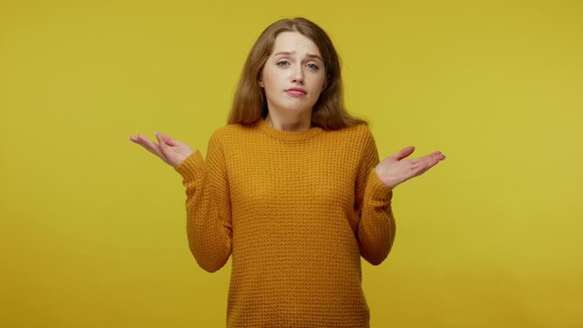 Clueless puzzled uncertain girl with brown hair in pullover gesturing i don't know, raising hands in bewilderment, looking confused, embarrassed, having no idea. indoor studio shot yellow background