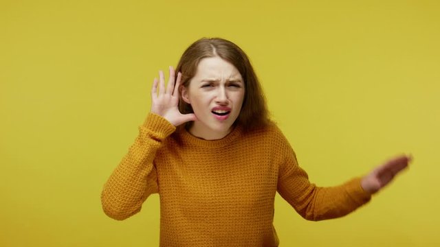 What? i don't listen! Annoyed girl holding arm near ear and pretending not to hear, showing bla bla hand gesture, uninterested in communication. indoor studio shot isolated on yellow background