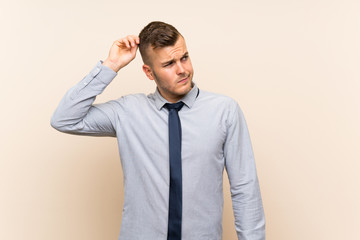 Young blonde businessman over isolated background having doubts and with confuse face expression