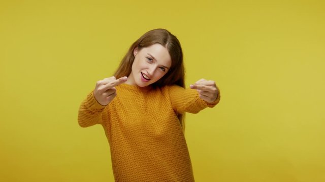 Positive girl in casual pullover showing middle fingers, trying to send off boring asshole with rude gesture and laughing at him, expressing disrespect. studio shot isolated on yellow background