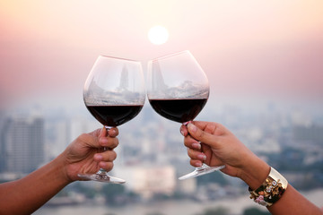 Hand of a lover's dinner is celebrated with red wine at a restaurant in a romantic atmosphere. Sunset and modern city background
