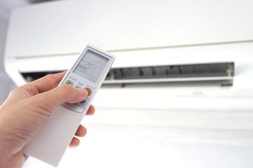 Man's hand using remote control open The air conditioner is cooled to 25 degrees Celsius in his...