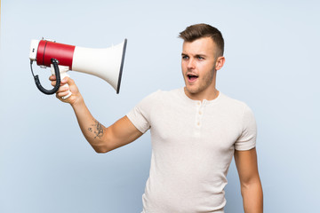 Young handsome blonde man over isolated blue background holding a megaphone