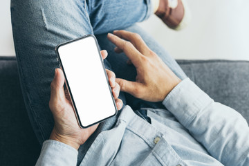 Mockup image blank white screen cell phone.men hand holding texting using mobile on sofa at home. background empty space for advertise text.people contact marketing business and technology