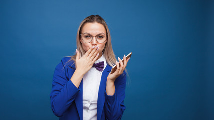 Cute and funny businesswoman in a stylish blue jacket and bow tie uses a smartphone.