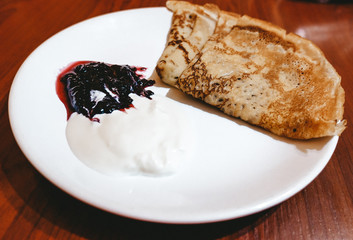 Appetizing fried pancakes with sour cream and jam on a white plate