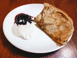 Appetizing fried pancakes with sour cream and jam on a white plate