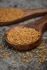 Fenugreek seeds in wooden spoon on textured background