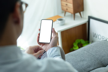 Mockup image blank white screen cell phone.man hand holding texting using mobile on sofa at home office.background empty space for advertise text.people contact marketing business,technology
