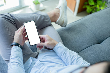 Mockup image blank white screen cell phone.man hand holding texting using mobile on sofa at home office.background empty space for advertise text.people contact marketing business,technology