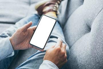 Mockup image blank white screen cell phone.man hand holding texting using mobile on sofa at home.background empty space for advertise text.people contact marketing business,technology