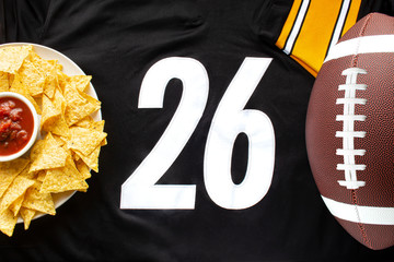An American football with organic nacho chips and mild salsa on a white black football jersey with the 26 number on horizontal view - Powered by Adobe