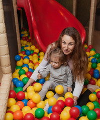 Fototapeta na wymiar Cheerful mom and little daughter are playing in the pool with colored balls in the children's entertainment center. Family holiday