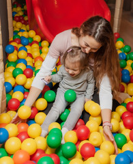 Fototapeta na wymiar Cheerful mom and little daughter are playing in the pool with colored balls in the children's entertainment center. Family holiday