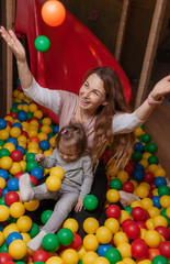 Cheerful mom and little daughter are playing in the pool with colored balls in the children's entertainment center. Family holiday
