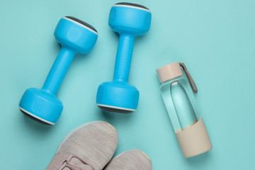 Flat lay style concept of healthy lifestyle, sport and fitness. Sports shoes for running, dumbbells, bottle of water on blue pastel background. Top view