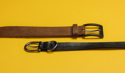 Two leather belts on yellow background close-up