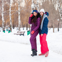 Portrait of two young beautiful women in ski suit posing in winter in the park