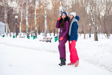 Fototapeta na wymiar Portrait of two young beautiful women in ski suit posing in winter in the park