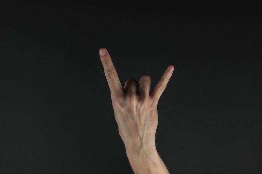Female hand shows a gesture of rock (horns) on a black background