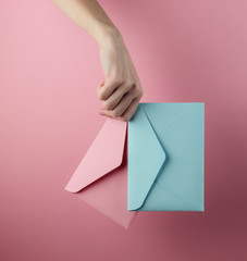 Female hand holds two envelopes on a pink pastel background
