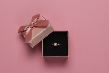 Gift box and engagement gold ring with diamond on pink pastel background. Wedding, romantic...
