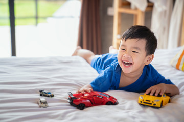 Asian boy fun and play a car toy on the bed