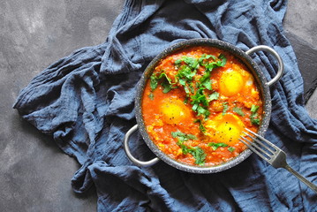 Shakshuka in pan on a gray rustic background.Middle eastern traditional dishes. Fried eggs with vegetables. Space for text. Top view.