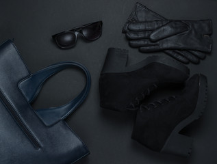 Women's fashion accessories on a black background. Suede boots, leather bag, gloves, sunglasses. Top view